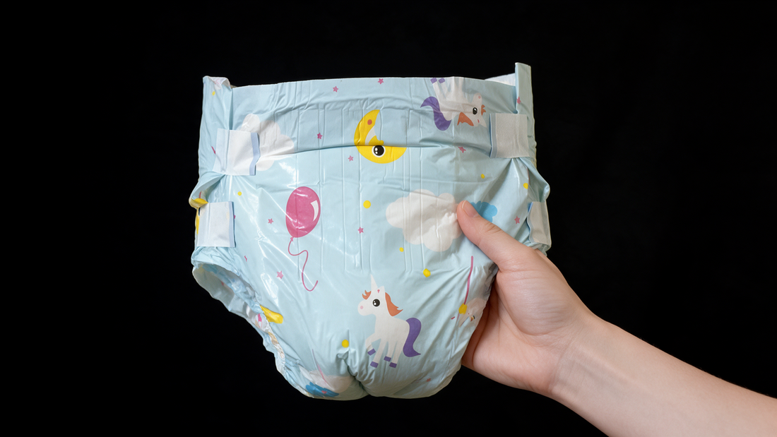 Hand holding an unworn light blue patterned diaper against a black background